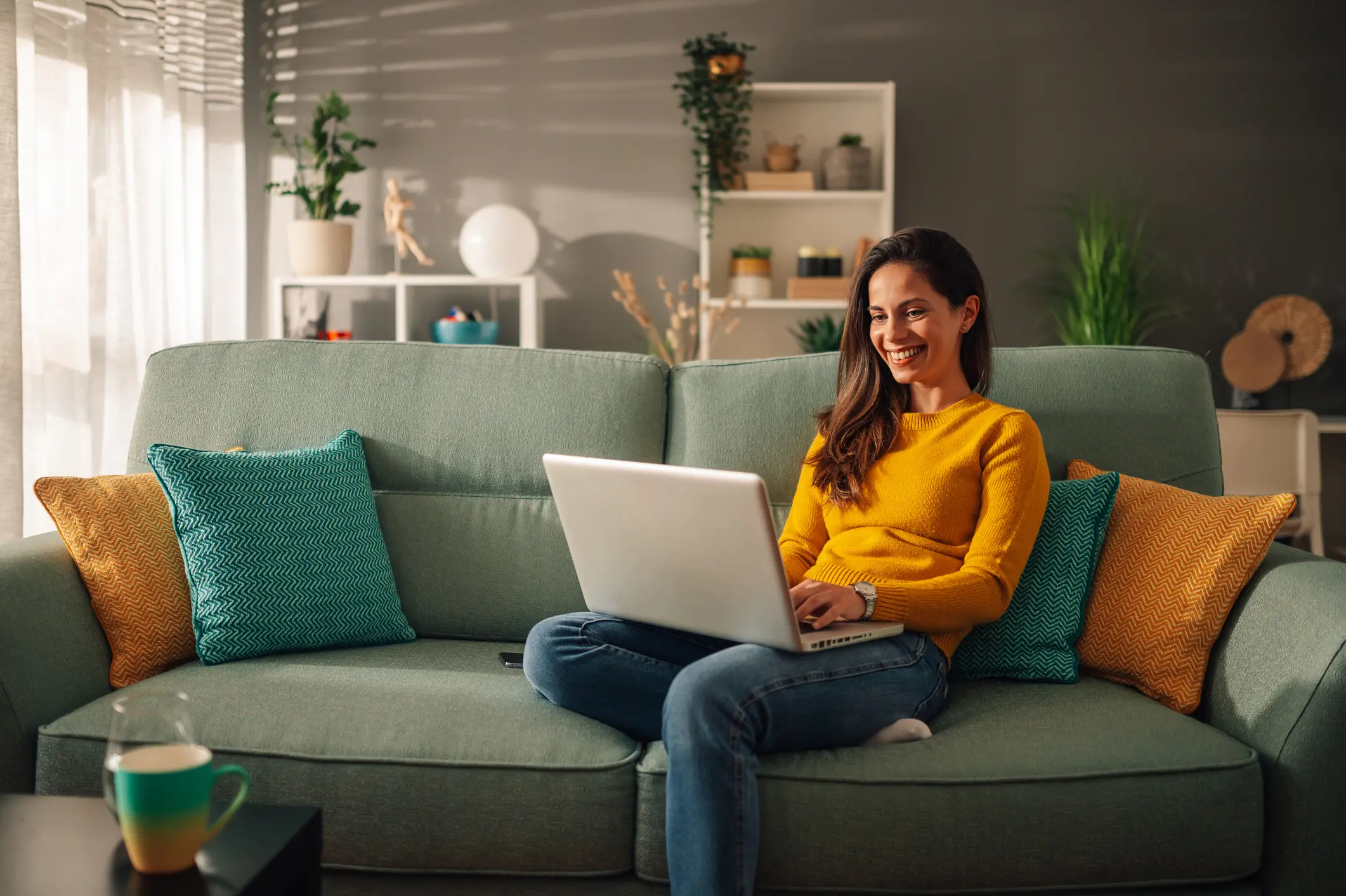 A woman in a yellow sweater using a laptop on a green couch.